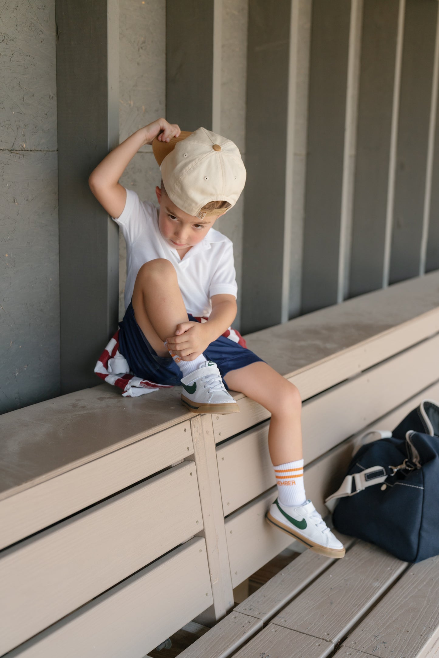 Child sitting on a bench wearing a cap, white shirt, and colorful shorts.