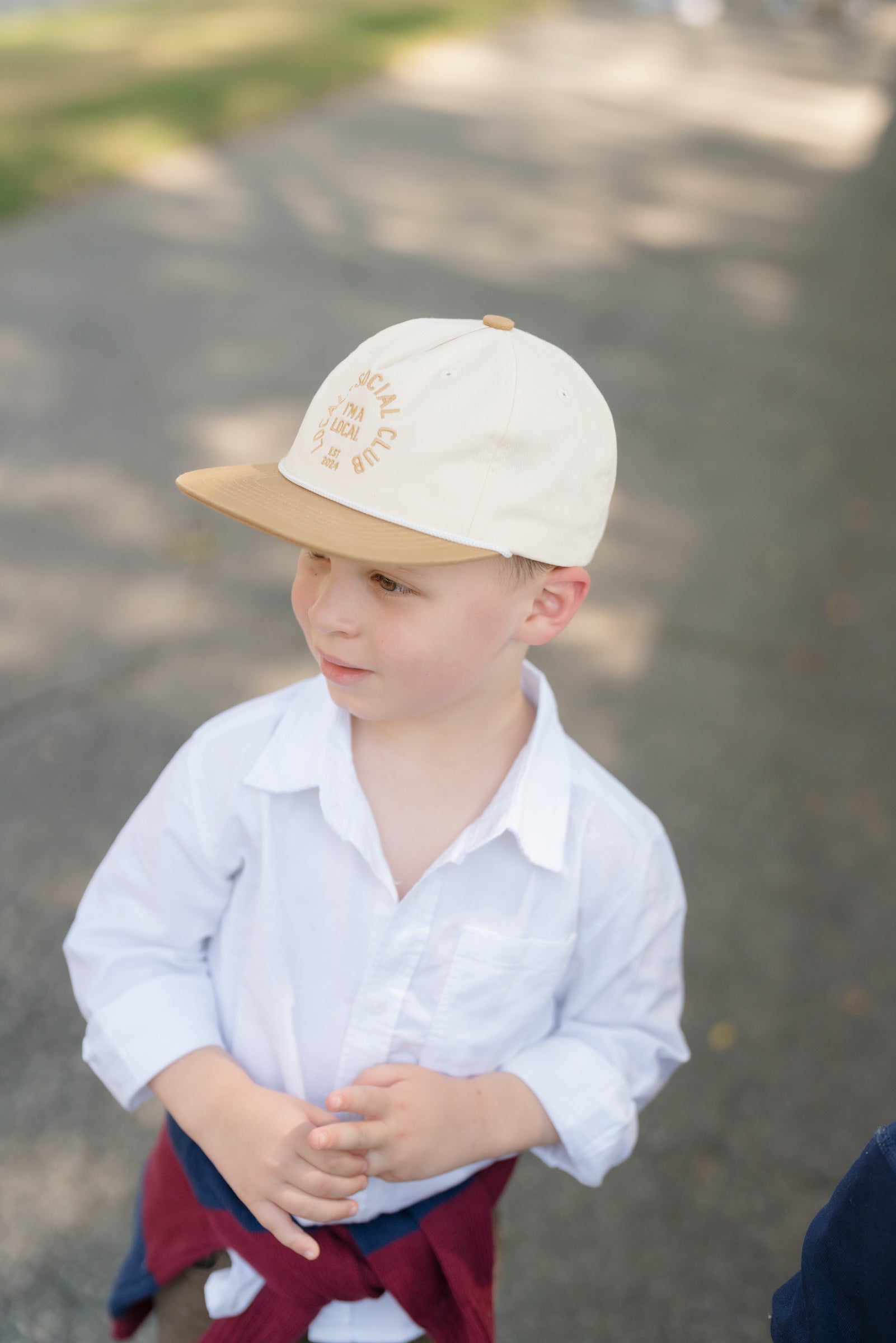 Child wearing a white shirt and beige cap on a blurred outdoor background